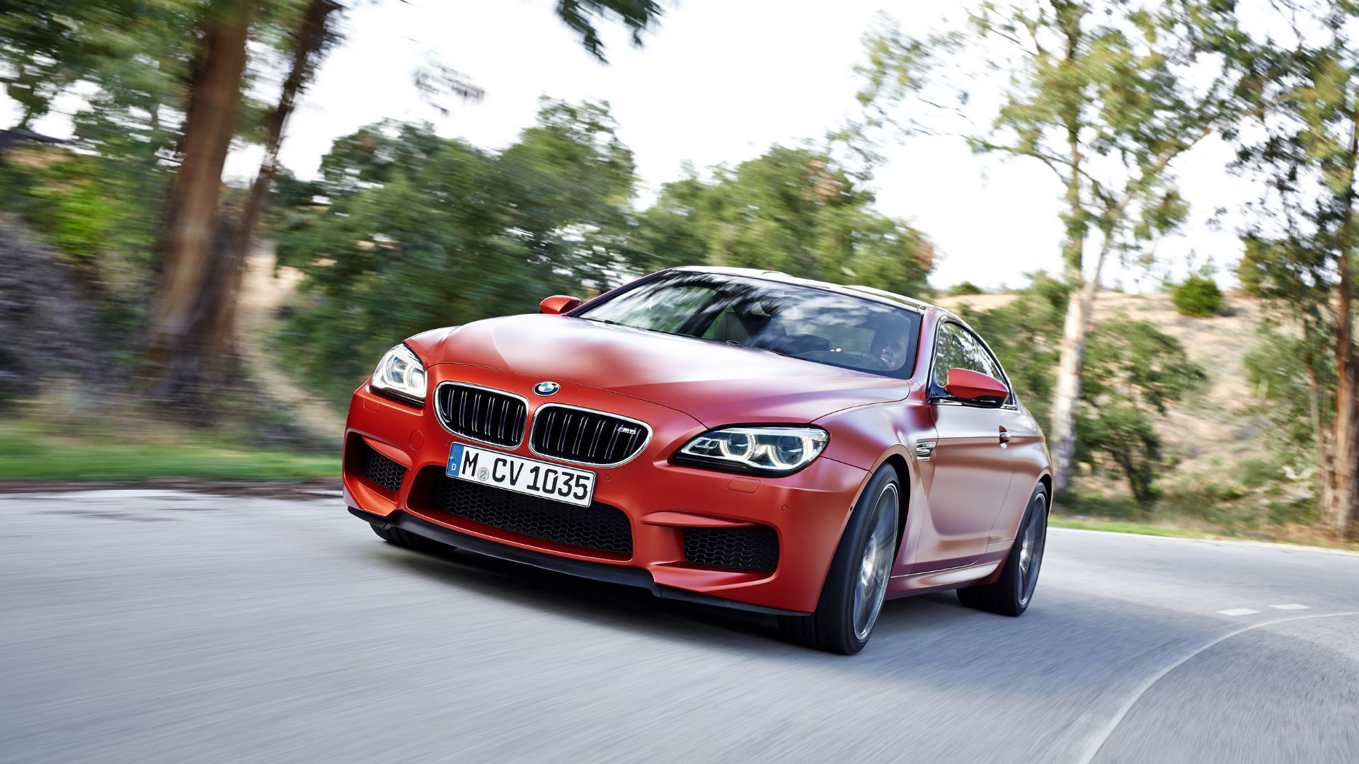 Orange BMW M6 Coupé driving on a winding country road.