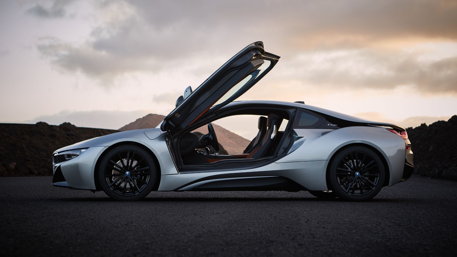 Side profil;e of a silver 2017 BMW i8 Coupe parked with its gull-wing doors up.