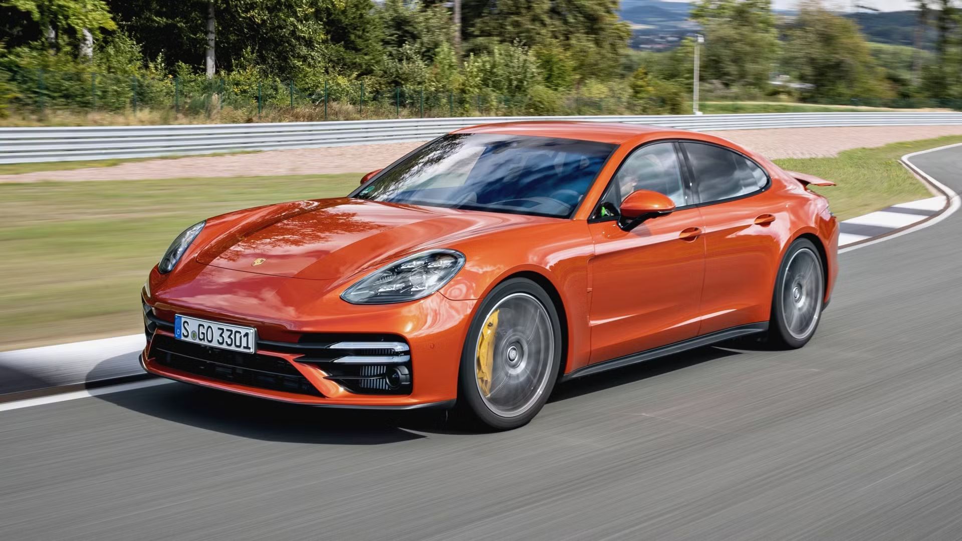 Full view of an orange 2021 Porsche Panamera Turbo S driving on a race track. 