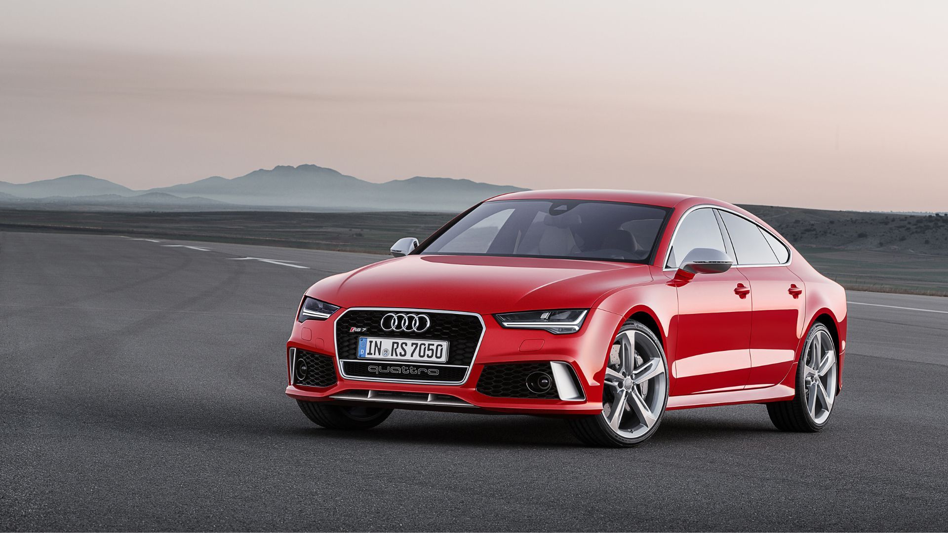 Full view of a red 2014 Audi RS7 parked on tarmac with mountains in the background.