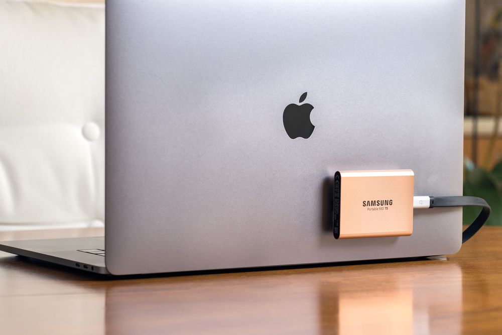 A Samsung T5 Portable SSD hard drive connected to a Macbook Pro secured with velcro tape.