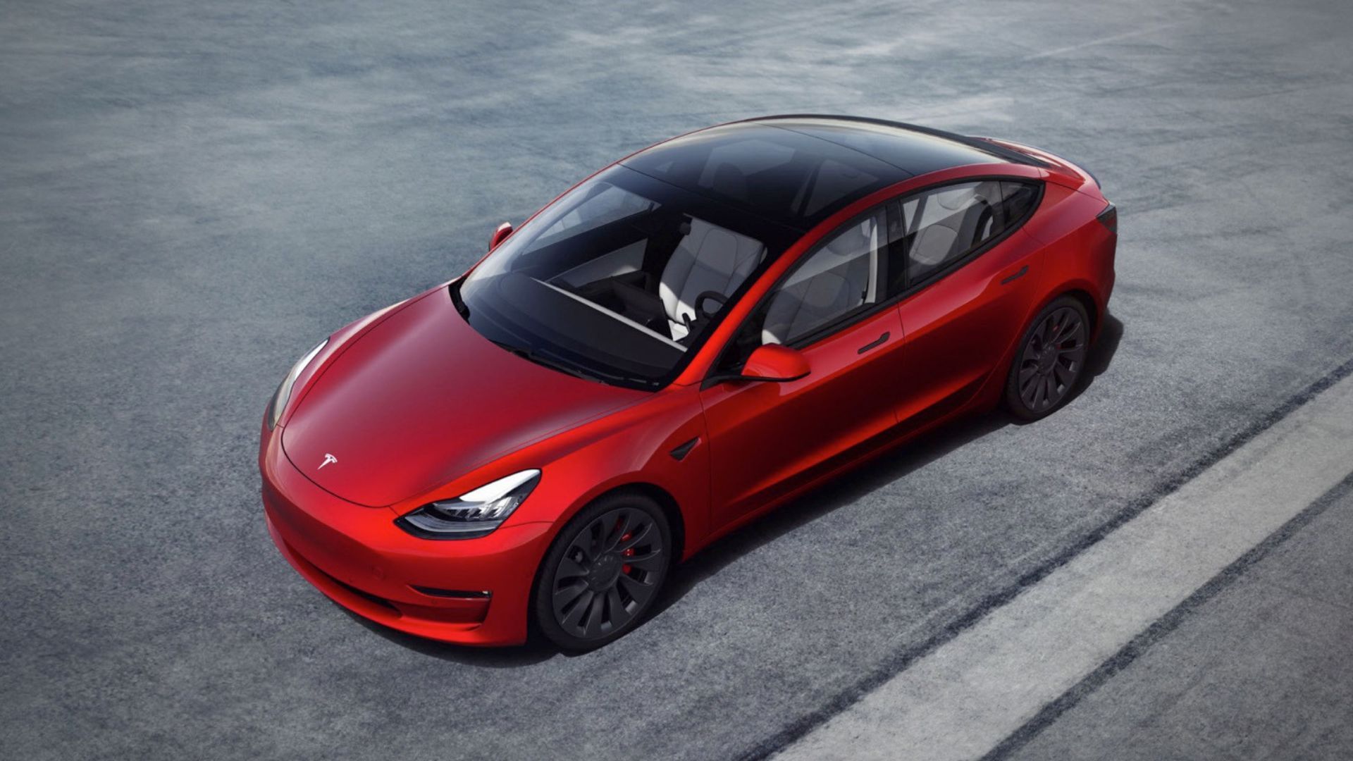 A red Tesla Model 3 parked on tarmac picture from above.