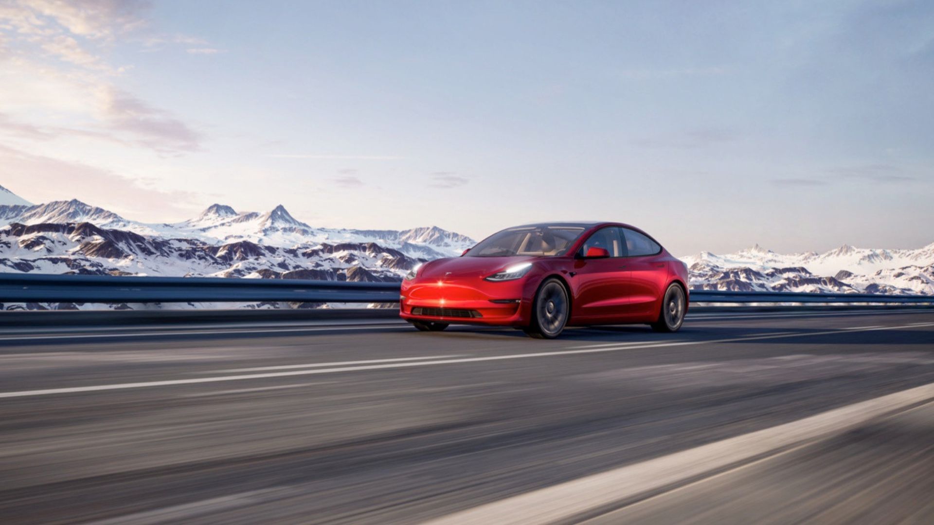 A red Tesla Model driving driving on a country road with snowcapped mountains in the background.