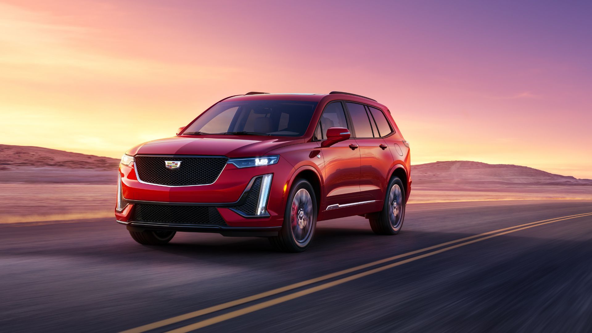 Front three-quarter view of a red 2024 Cadillac XT6 driving on a road through the desert.