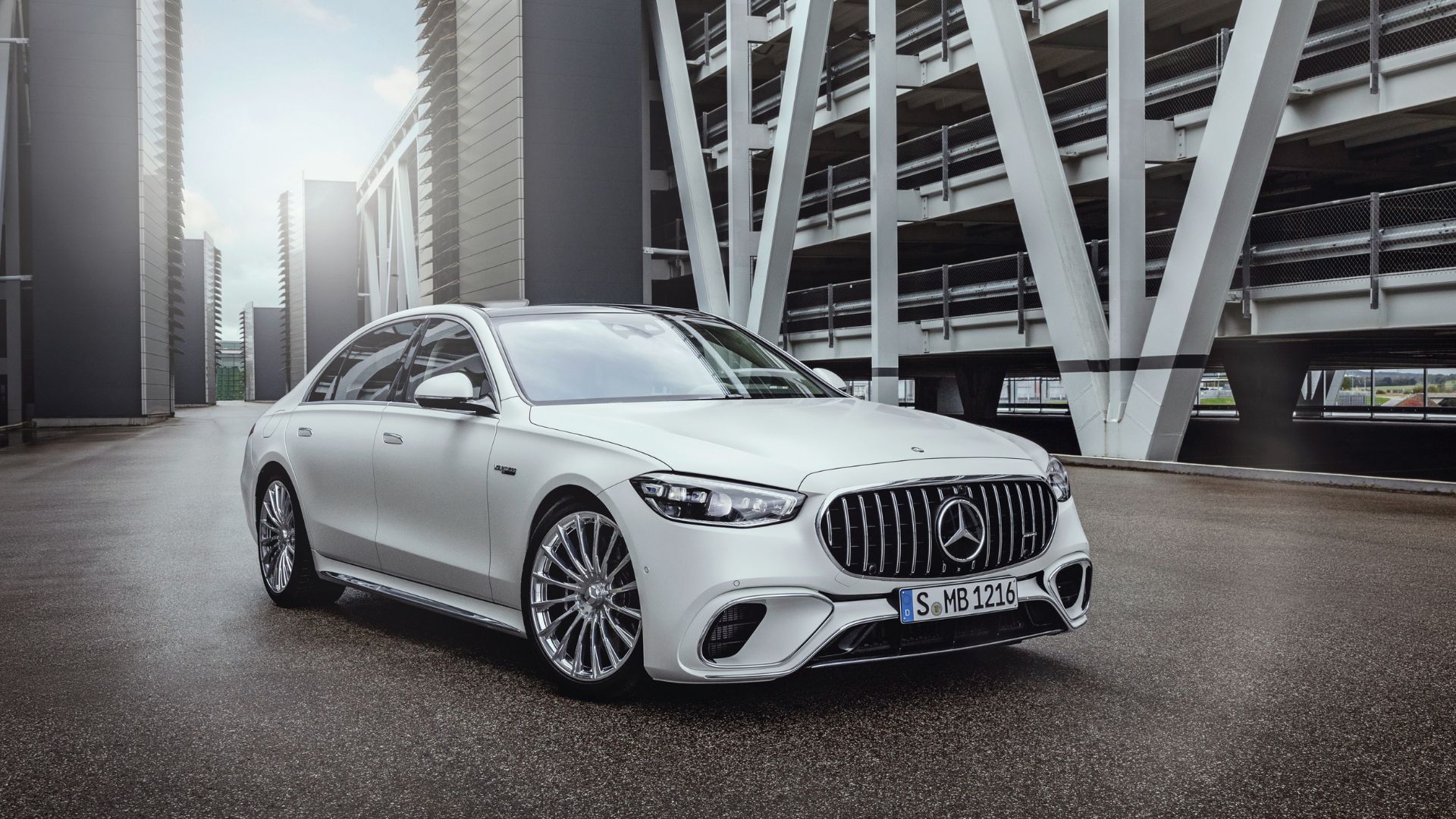 Full view of a white 2025 Mercedes-AMG S 63 E PERFORMANCE parked on tarmac in between buildings.