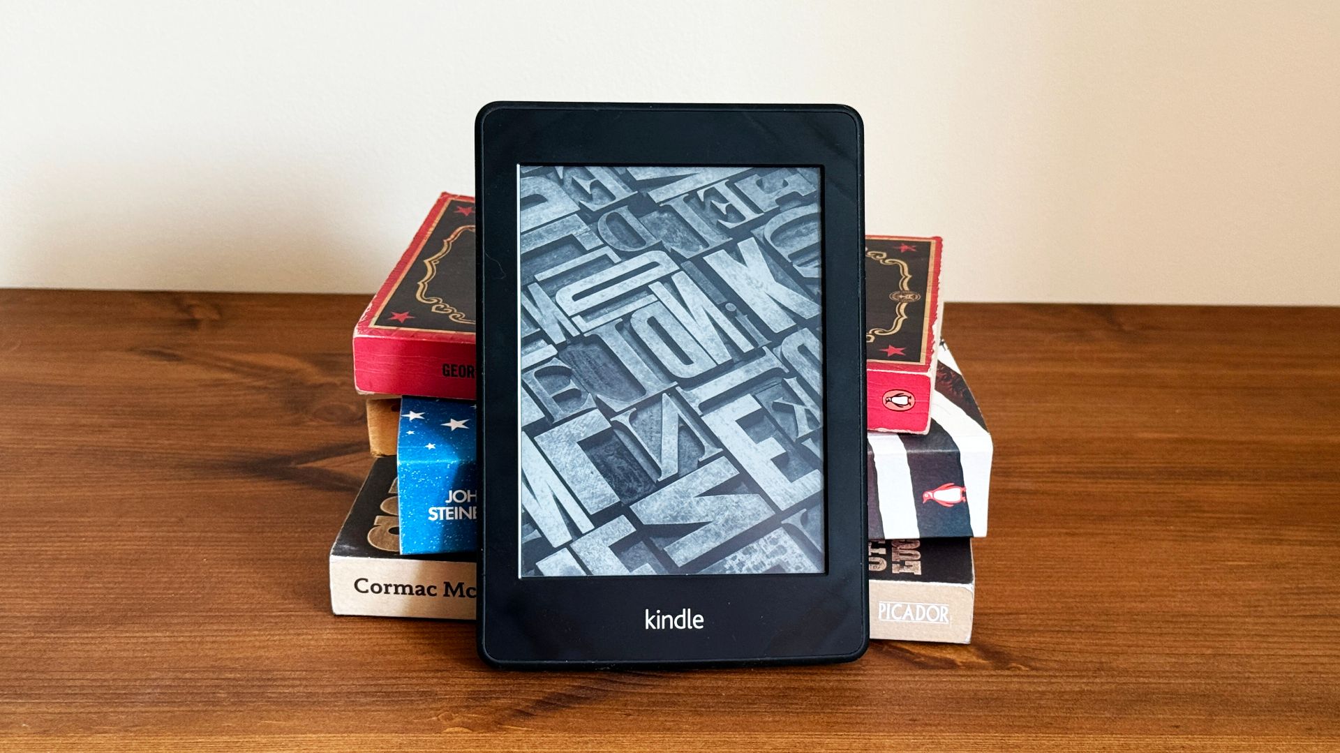 A stack of paper books with a Kindle eReader in front of them.