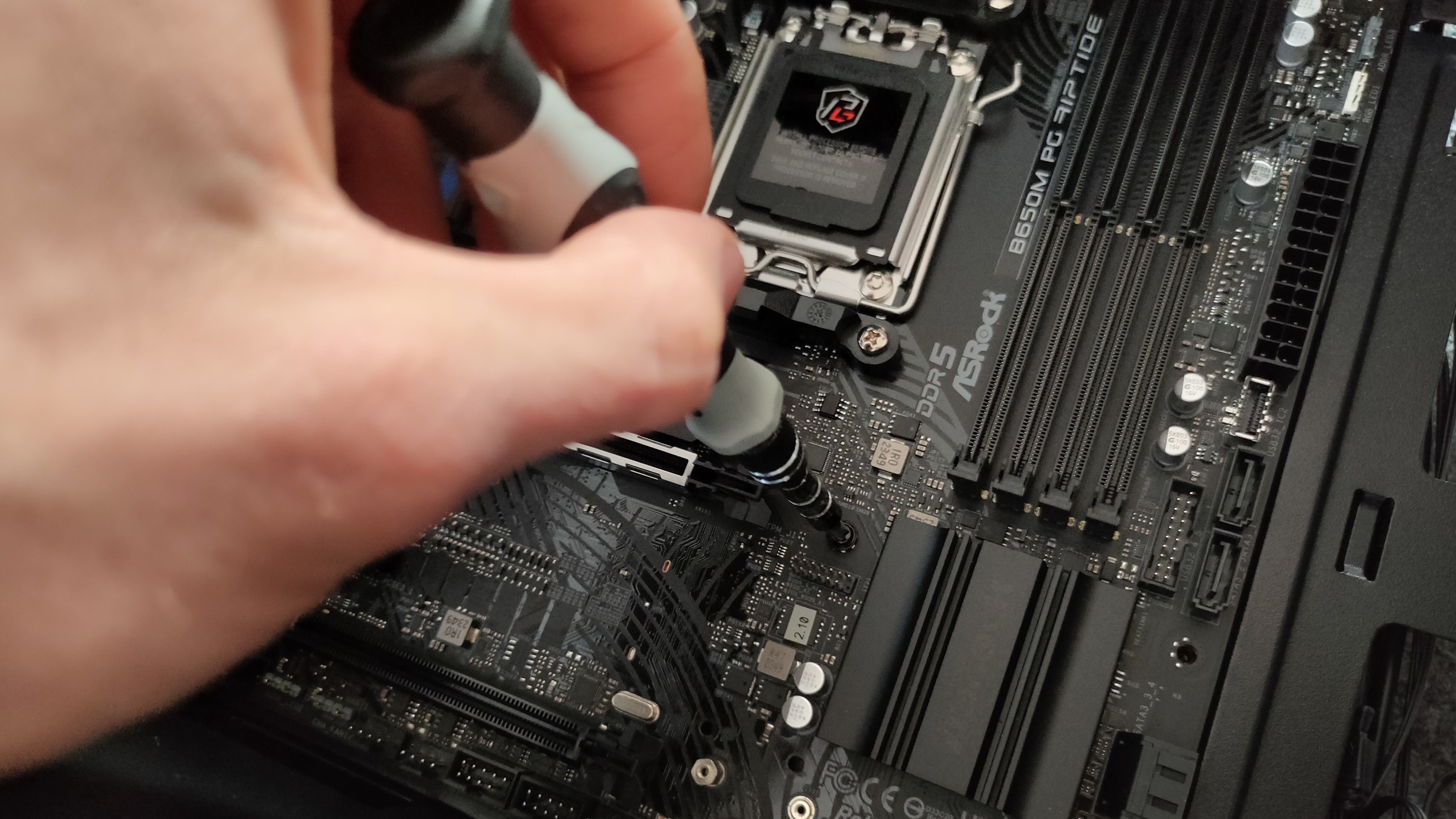 A hand screwing a motherboard into a PC case.