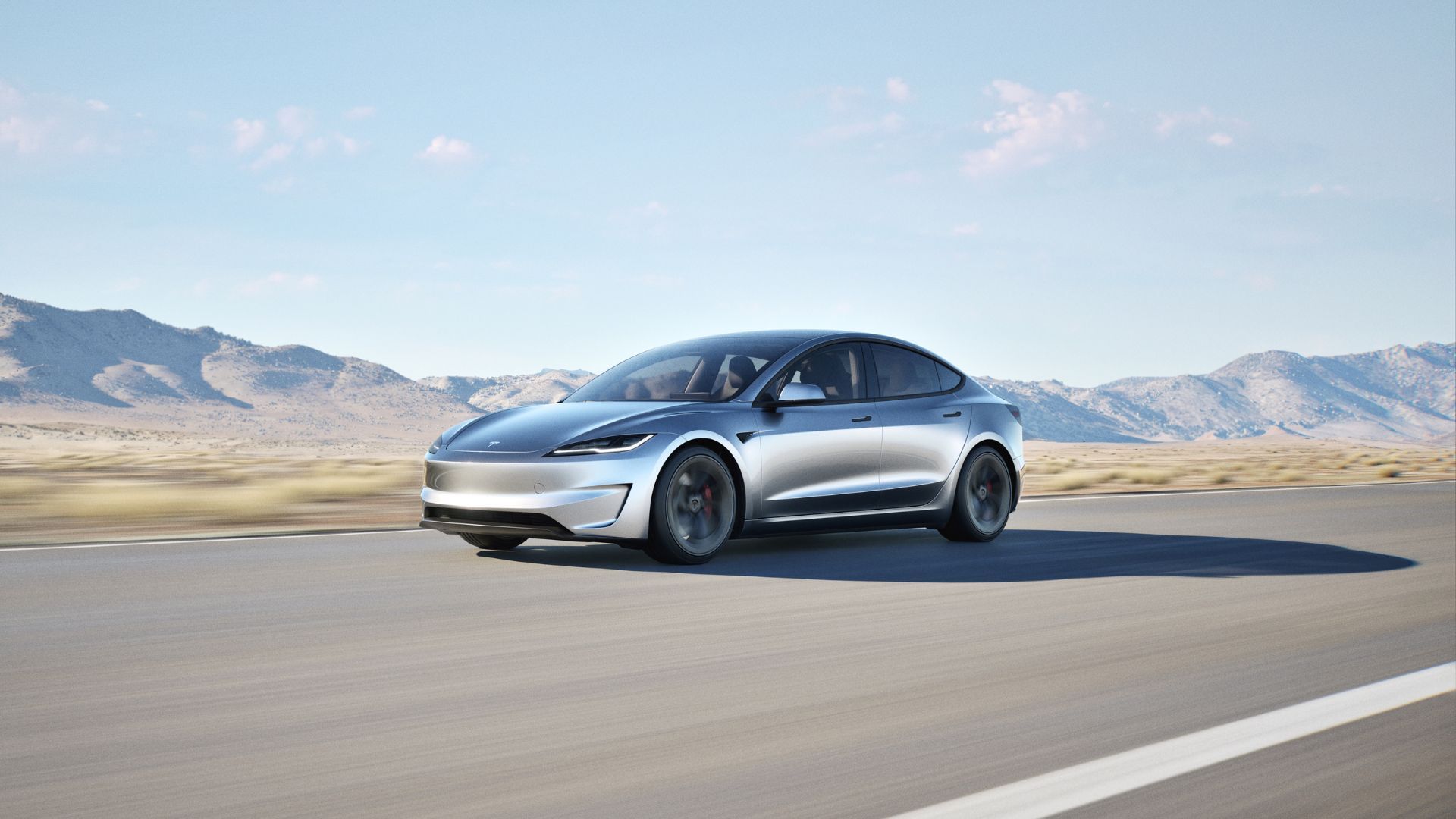 Full view of a silver Tesla Model 3 Performance driving on a country road with mountains in the background.