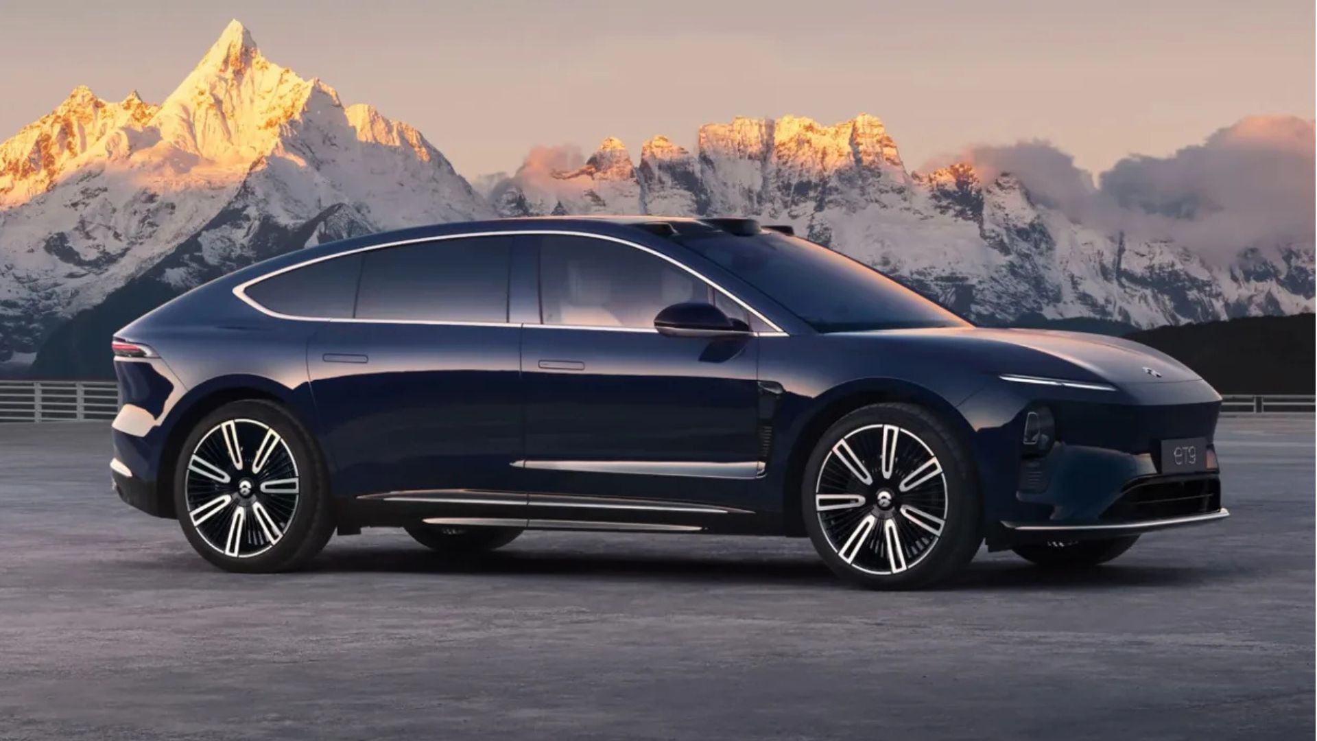 Side profile view of a black Nio ET with snow-capped moutains in the background.