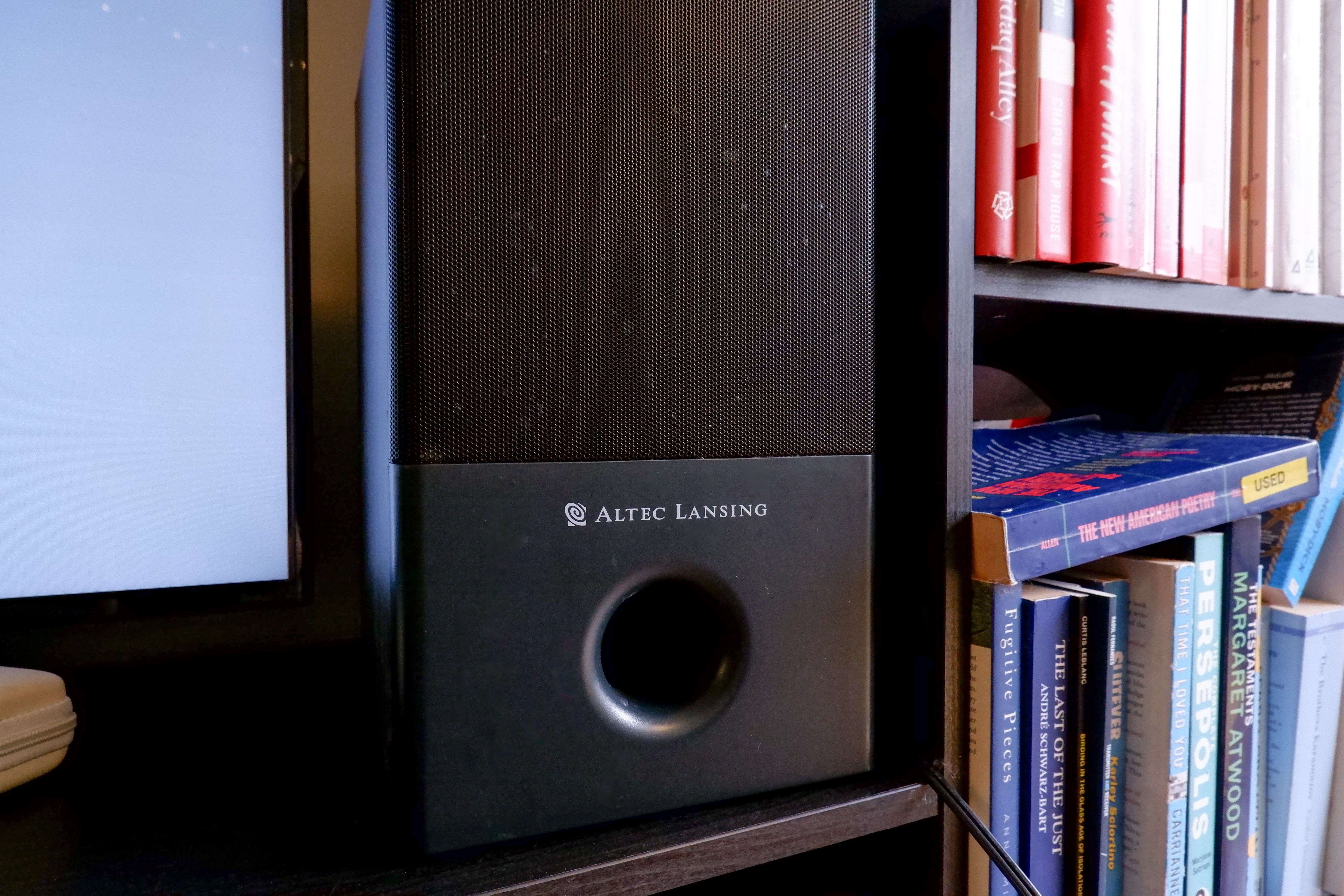 A subwoofer on black media console, next to a book shelf.