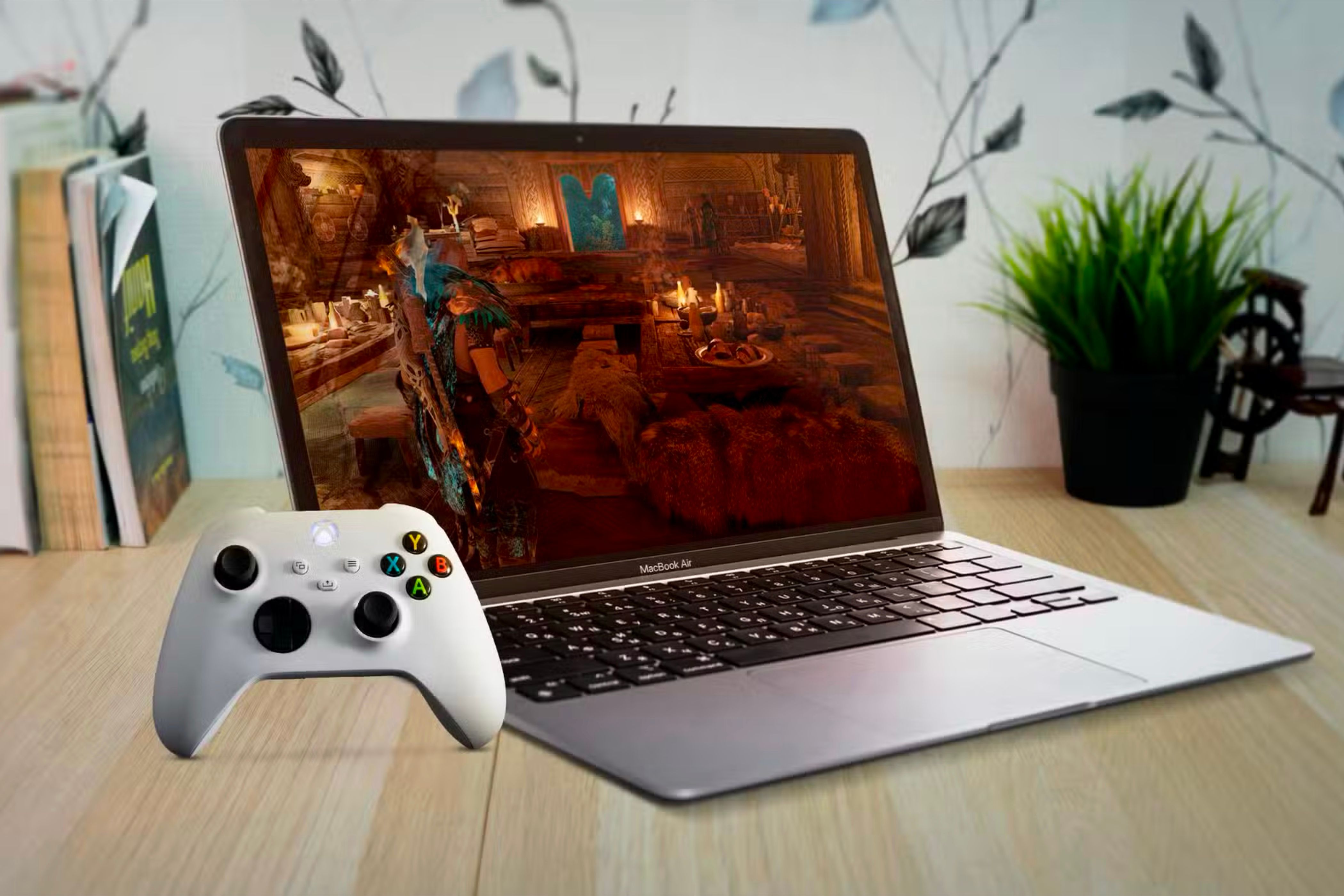 A MacBook Air under a wooden table with a game on the screen and an Xbox controller on the left.