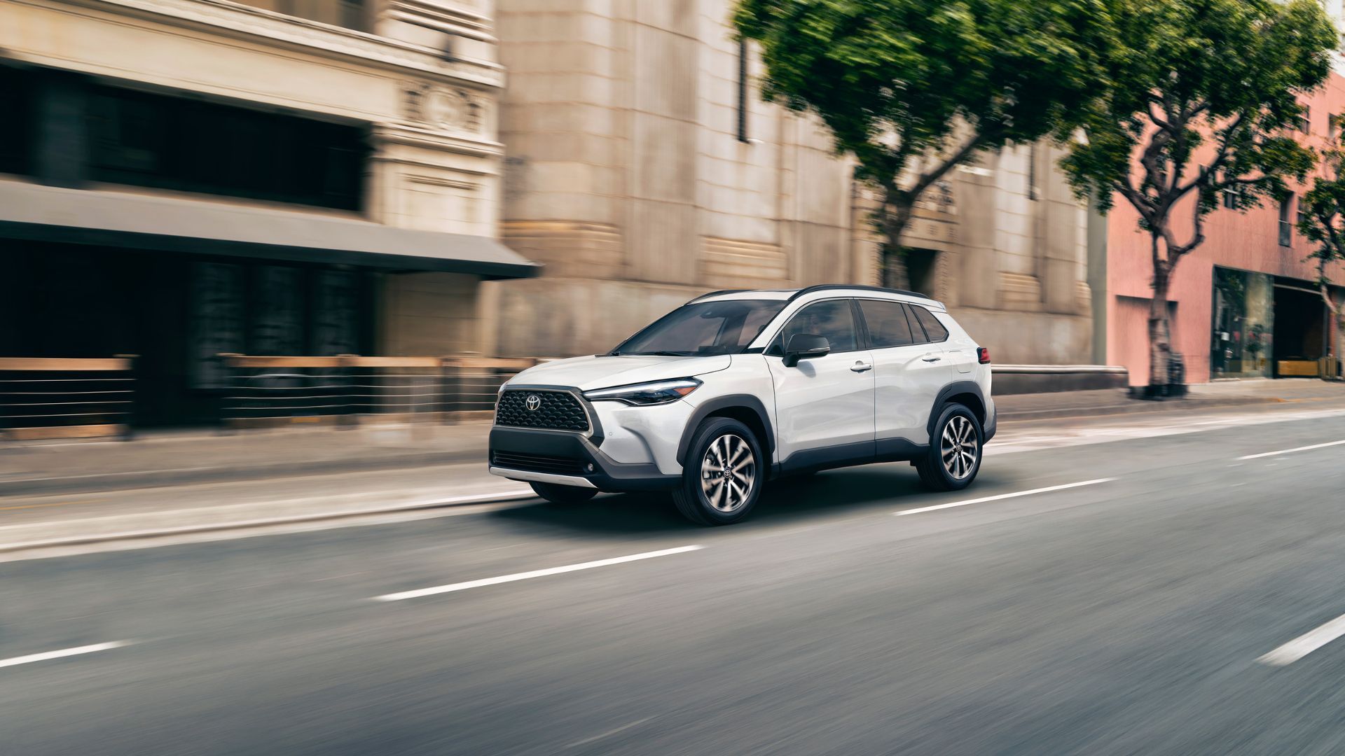 Динамичный вид спереди под углом 3/4 белого Toyota Corolla Cross Hybrid XSE 2025 года, движущегося в городском потоке