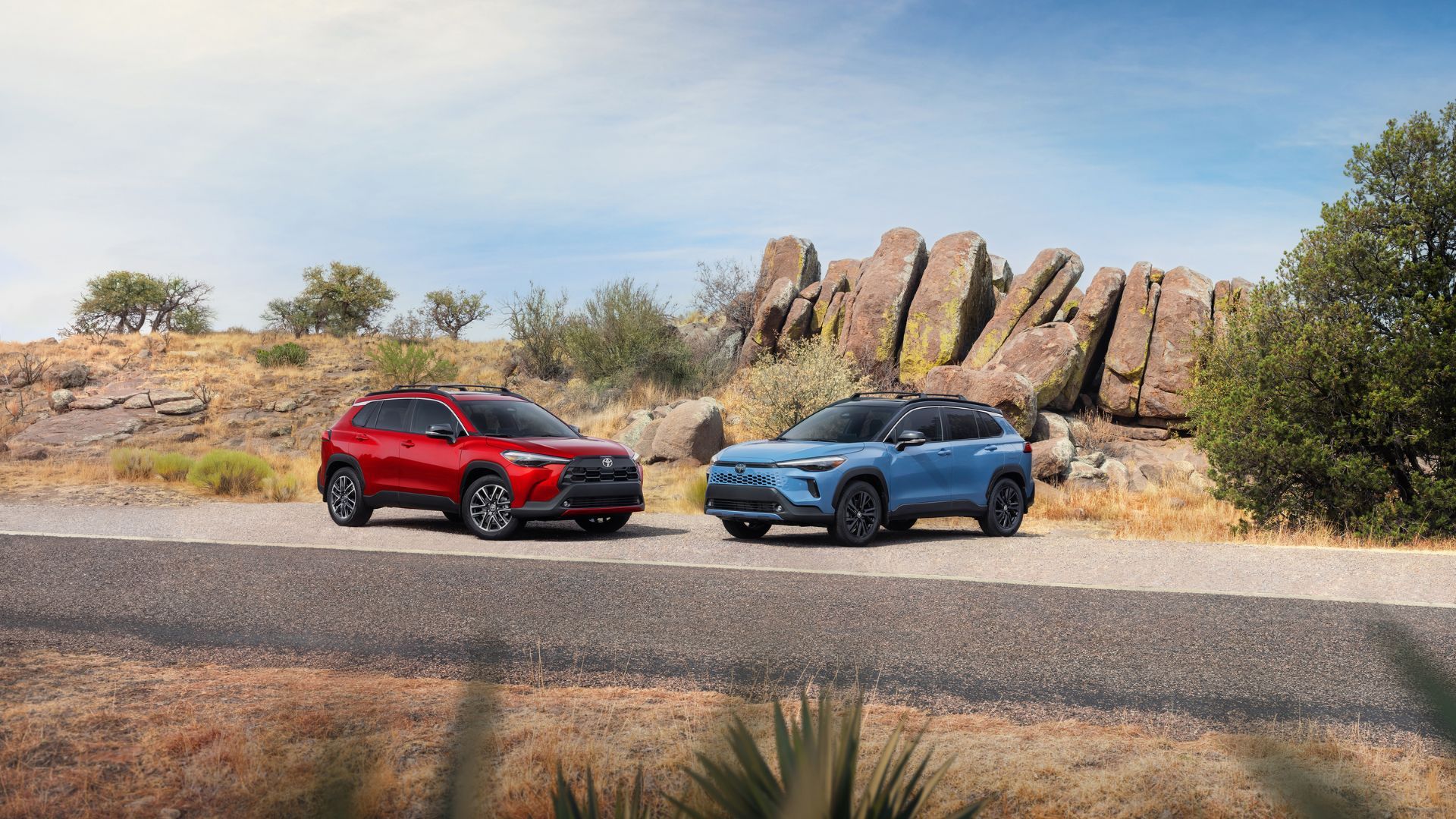 The static shot of two 2026 Toyota Corolla Cross SUV was parked next to each other in the desert with large rocks.