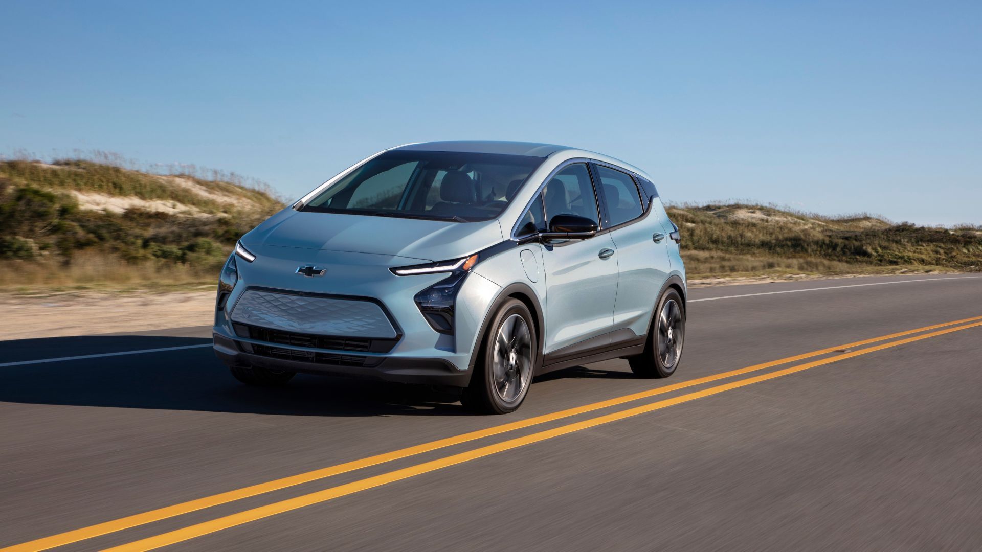 Dynamic front 3/4 shot of a silver 2022 Chevrolet Bolt EV driving on a country road.