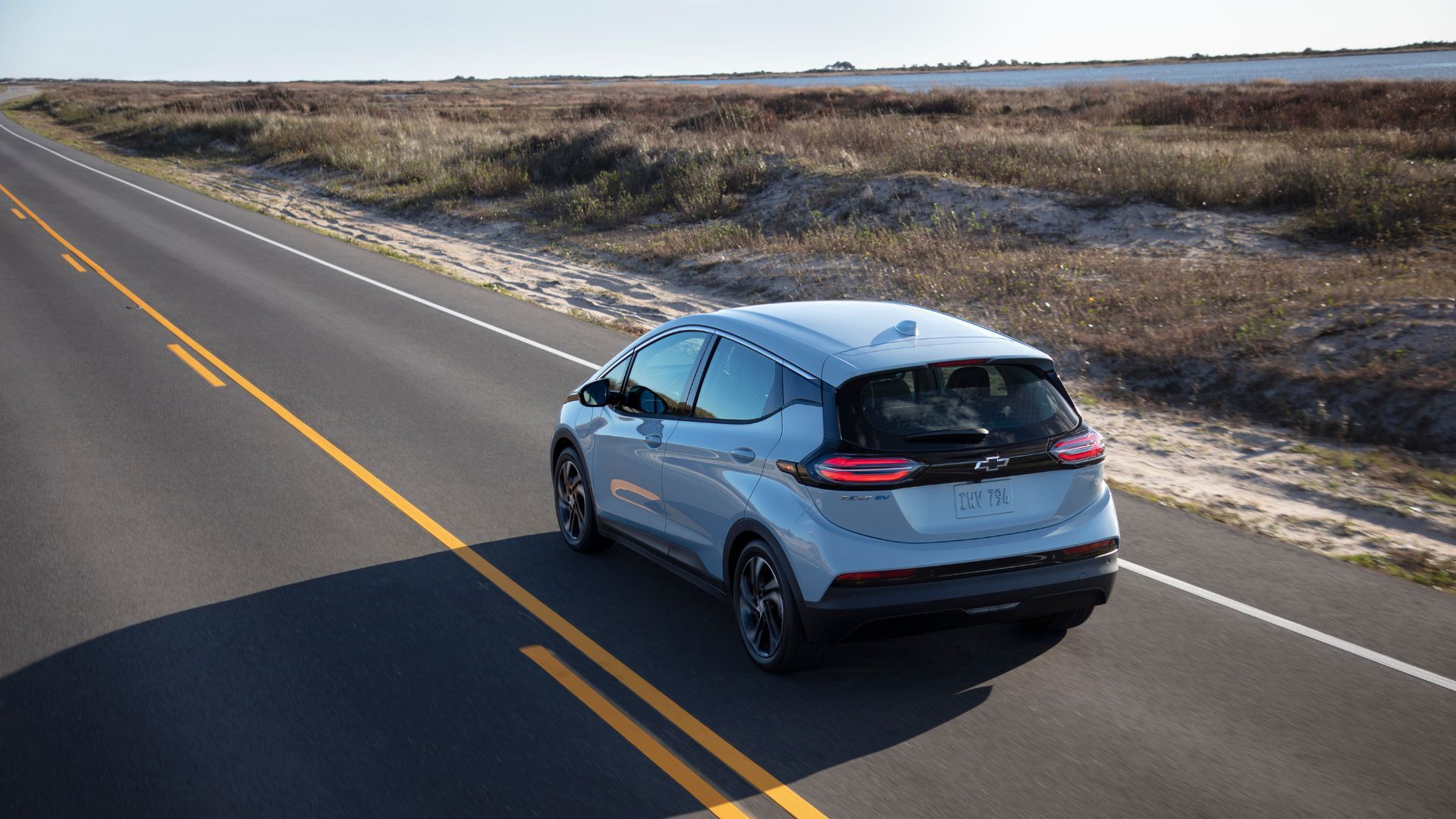 Dyanmic rear 3/4 shot of a silver 2022 Chevrolet Bolt EV driving on a country road.