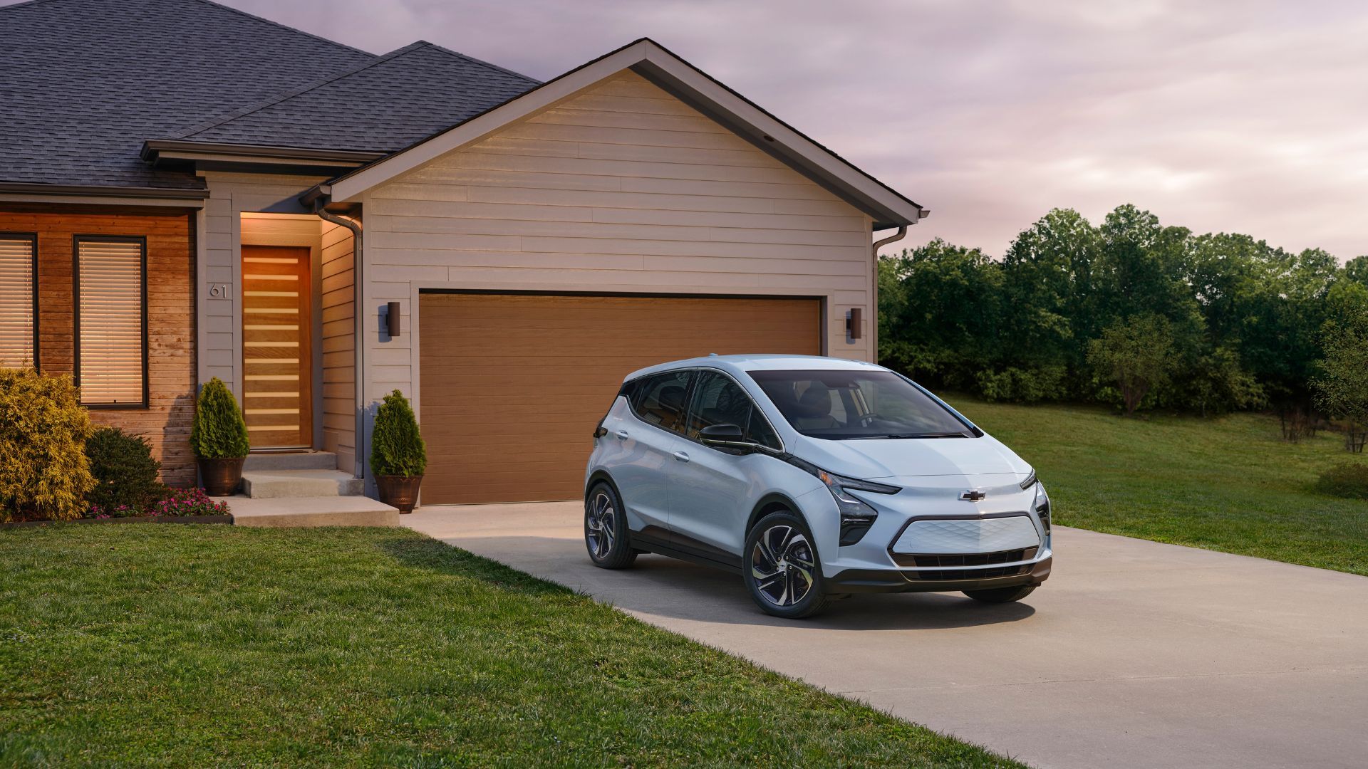 Static front 3/4 shot of a light blue 2023 Chevrolet Bolt EV parked on the driveway outside a house.