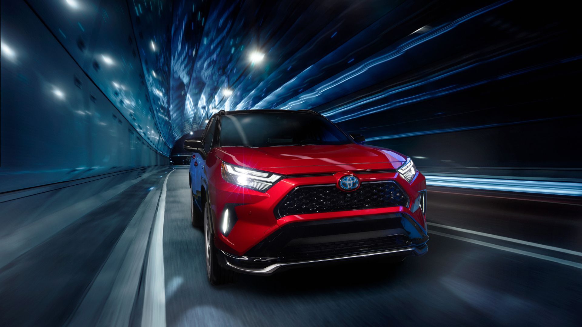 Dynamic front-end shot of a red 2024 Toyota RAV4 Prime XSE driving through a tunnel at night.