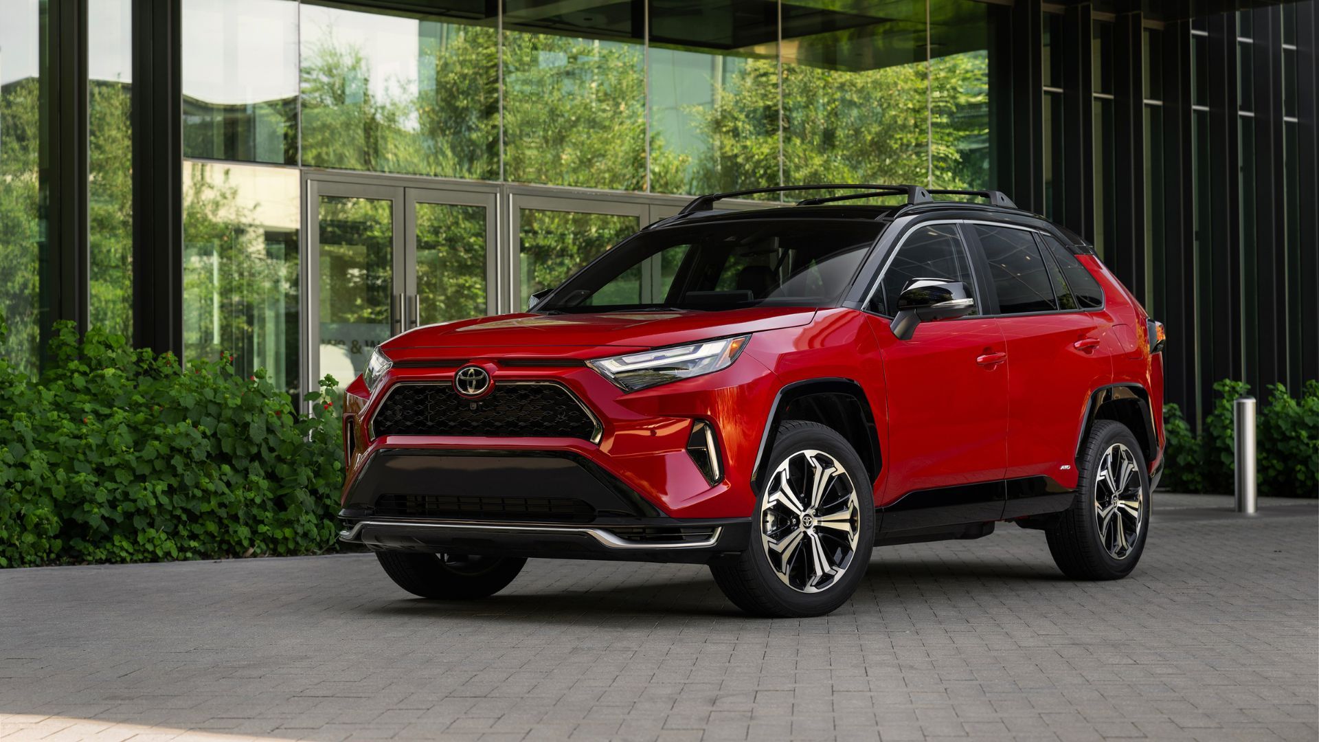 Static front 3/4 shot of a red 2025 Toyota RAV4 PHEV XSE parked outside of a modern building.