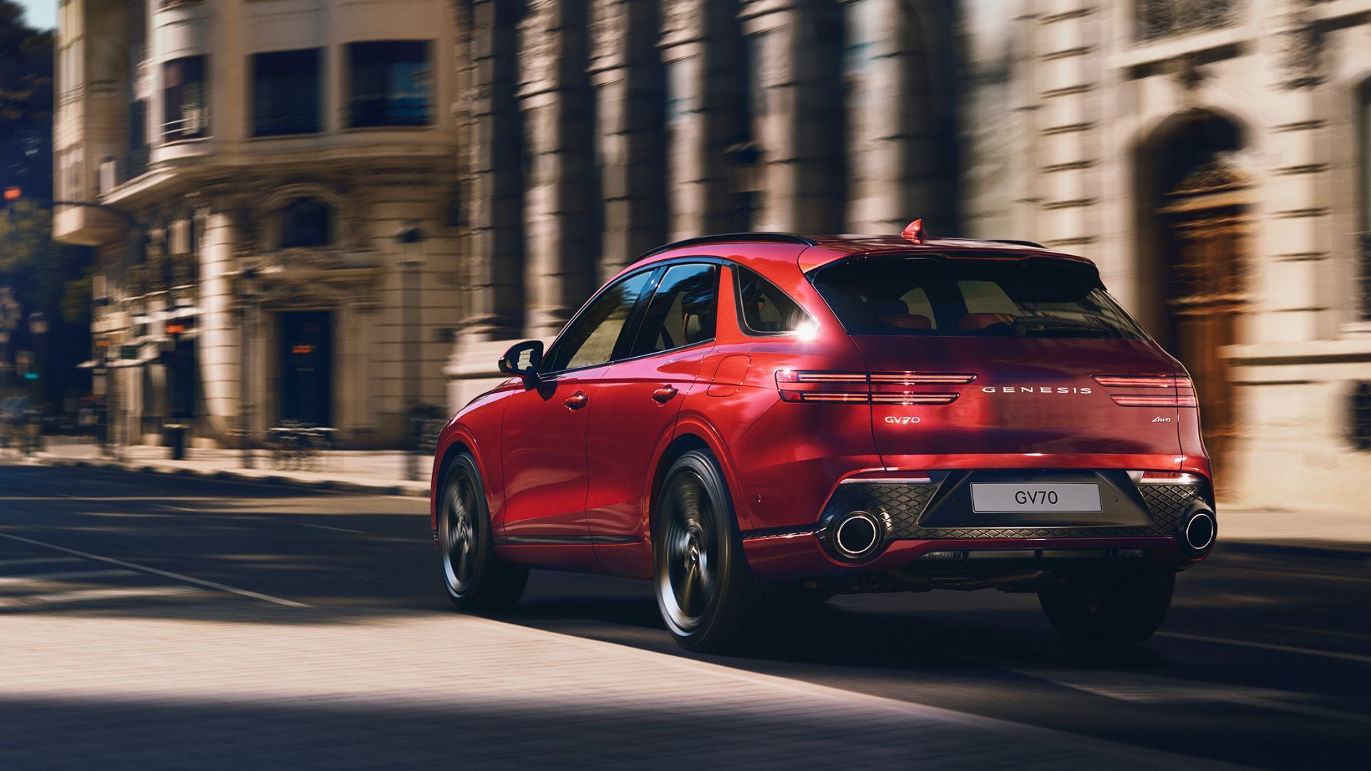Dyanmic rear 3/4 shot of a red Genesis GV70 driving through a city.