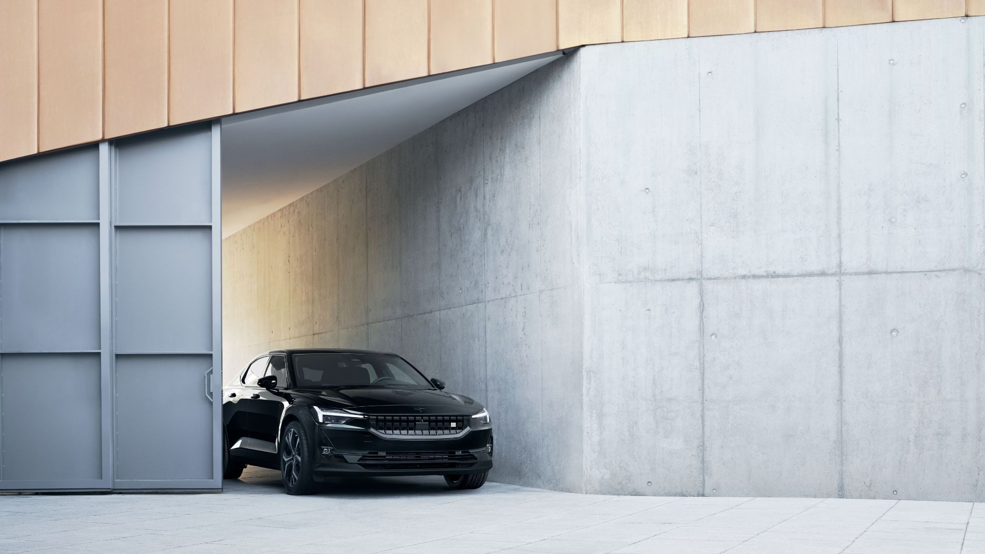 Static front-end shot of a black 2023 Polestar 2 parked between two buildings.