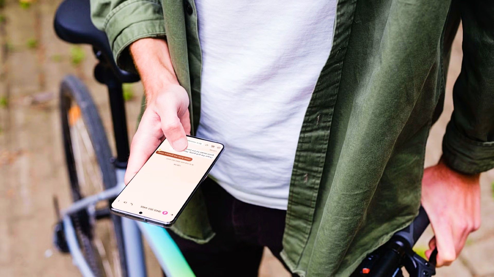 A person standing next to a bike holding their android device. There is a text conversation on the phone.