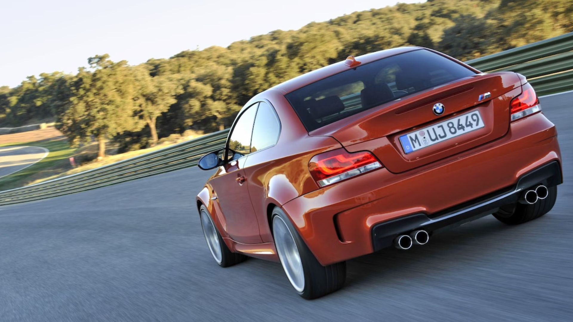 Dynamic rear 3/4 shot of an orange BMW 1M driving on a racetrack.