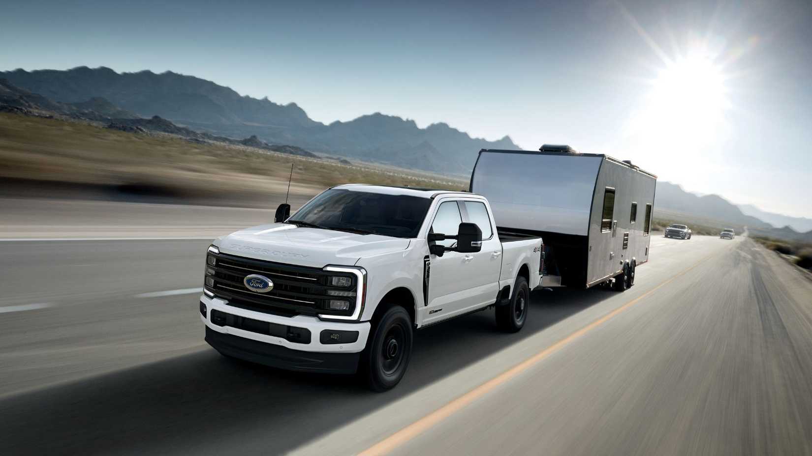 Dynamic front 3/4 shot of a white 2025 Ford F-350 Super Duty Platinum towing a trailer with mountains in the background.