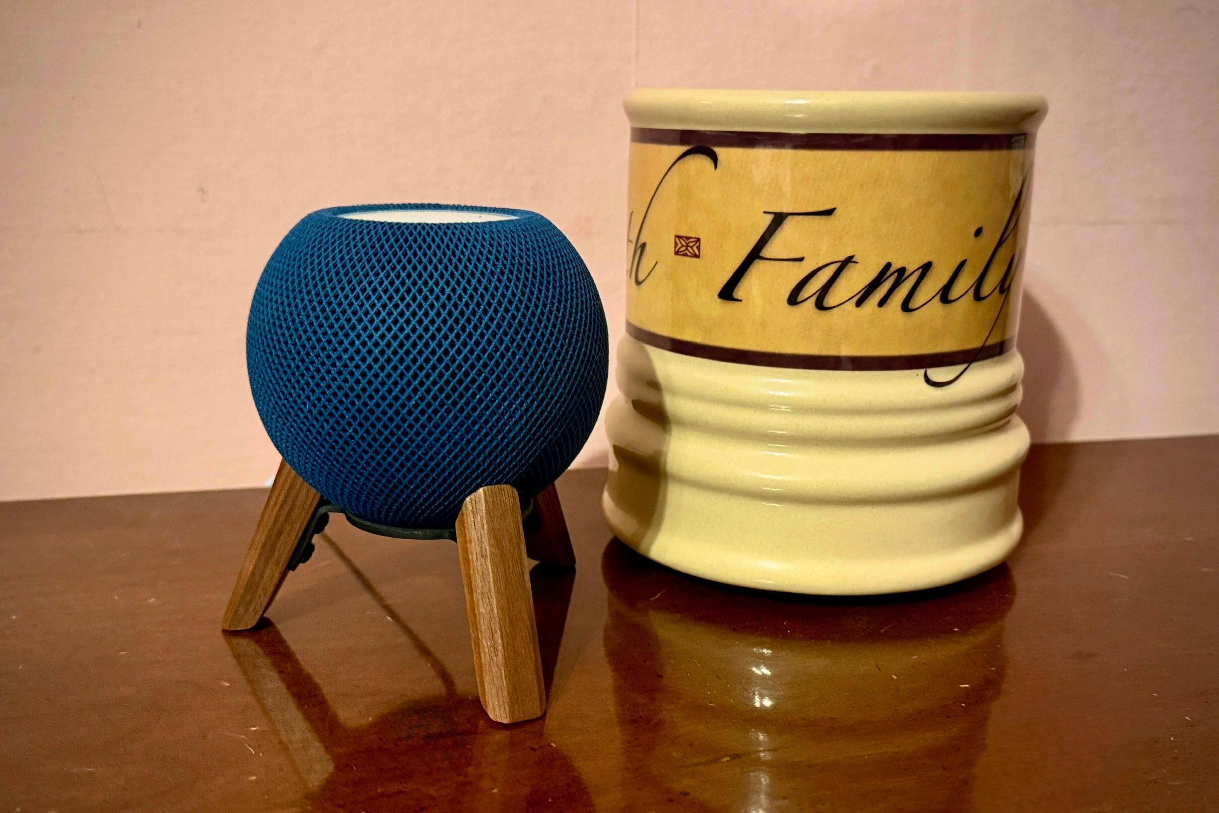 Blue HomePod Mini em um suporte de madeira ao lado de uma vela em uma superfície de madeira.
