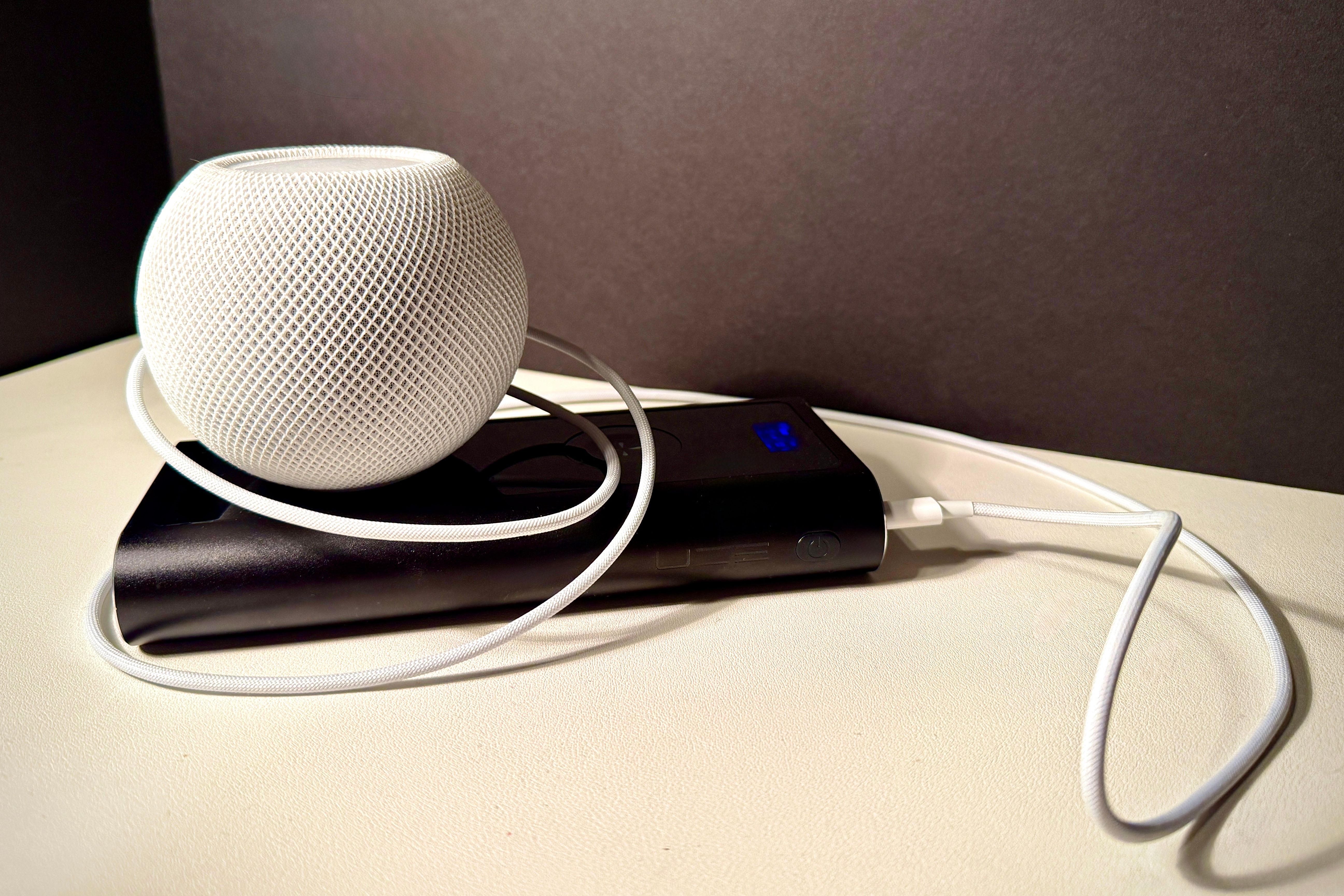 Mini HomePod branco conectado a um banco de energia para uso portátil.