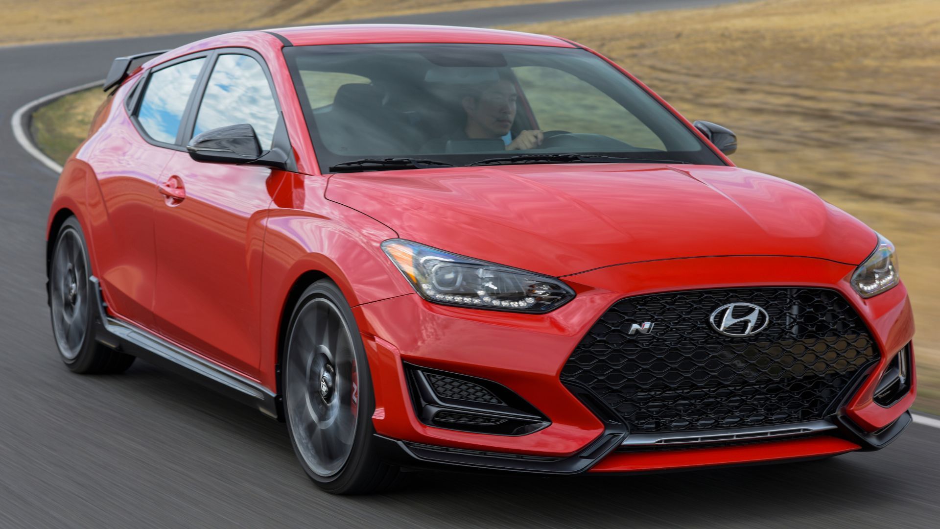 Dynamic front 3/4 shot of a red 2022 Hyundai Veloster N driving on a winding country road.