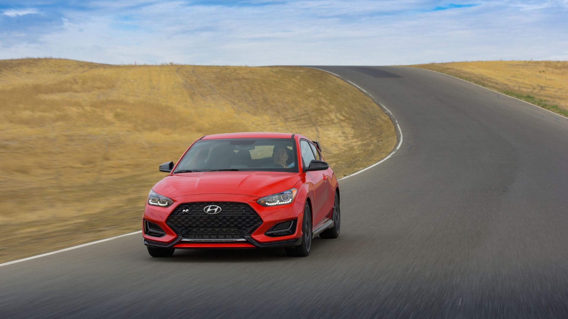 Dynamic front 3/4 shot of a red 2022 Hyundai Veloster N drivinh on a country road.