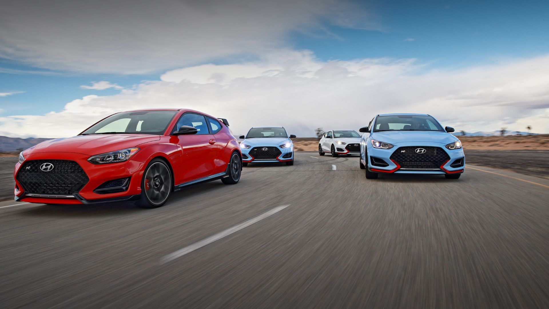 Four 2022 Hyundai Veloster N vehicles driving on a country road.