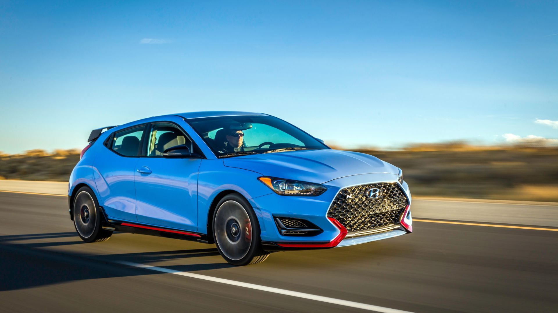 Dynamic front 3/4 shot of a blue 2022 Hyundai Veloster N driving on a country road.