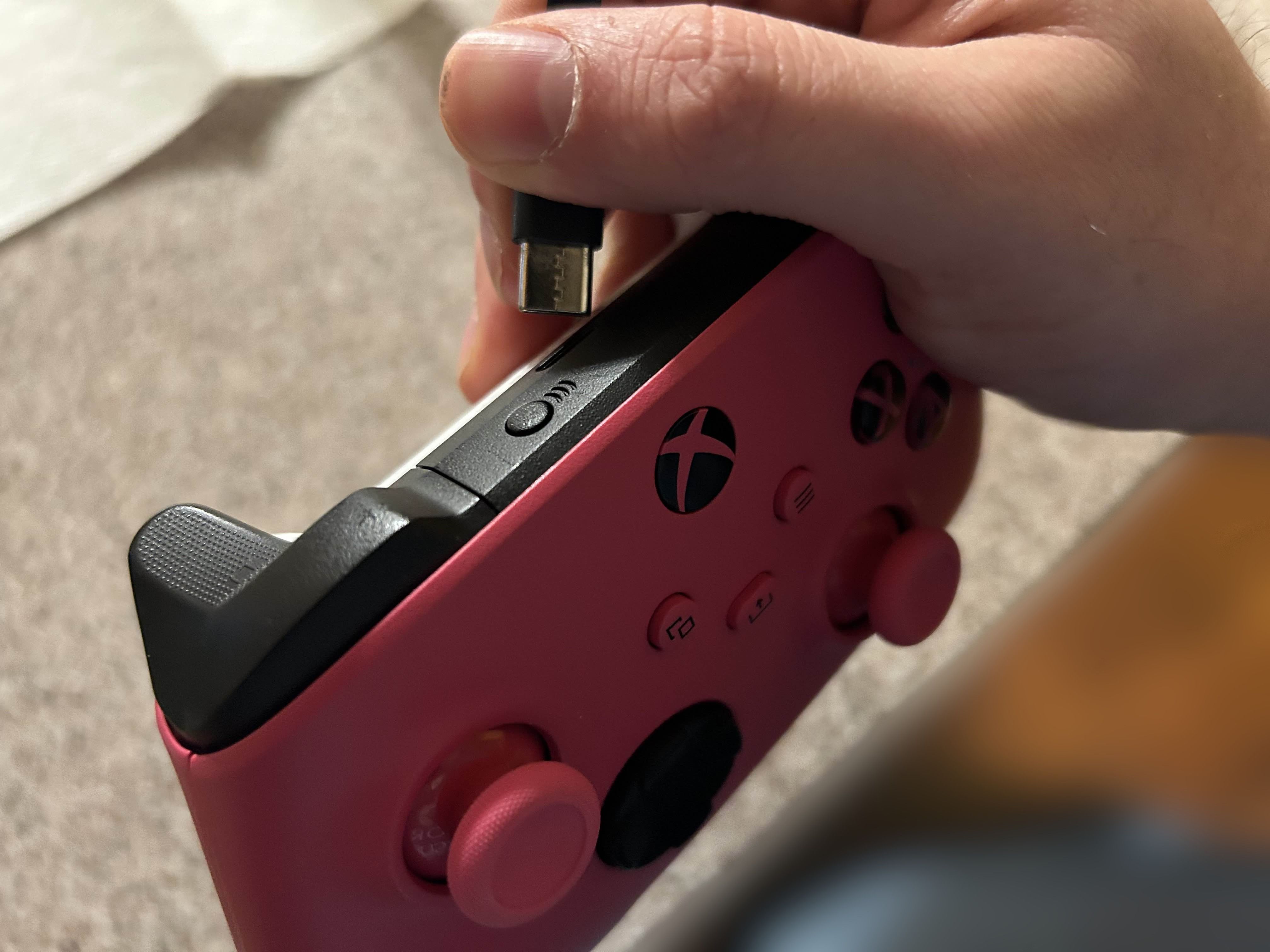 An pink Xbox One Controller that is about to be plugged in with its power cable.