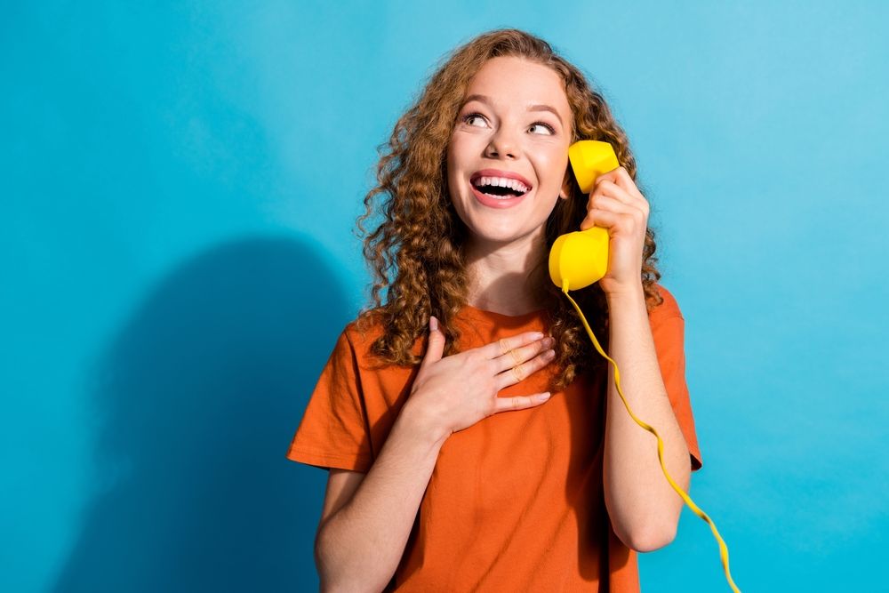 A woman holding an old-fashioned yellow telephone.