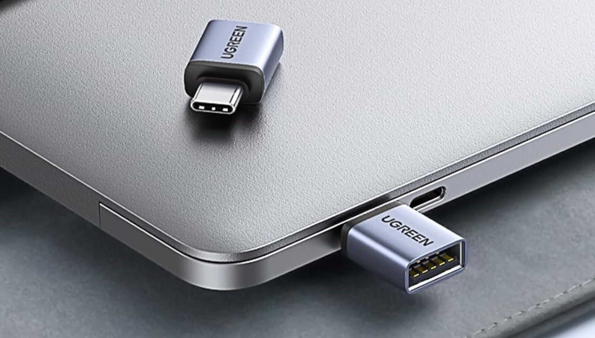 Two UGREEN USB-C to USB-A Adapters, one sitting on top of a laptop and one connected to said laptop.