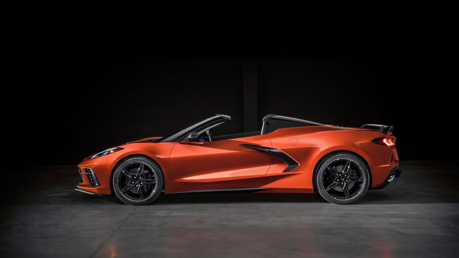 Side profile shot of an orange 2020 Chevrolet Corvette Stingray Convertible in a studio with a black backdrop.