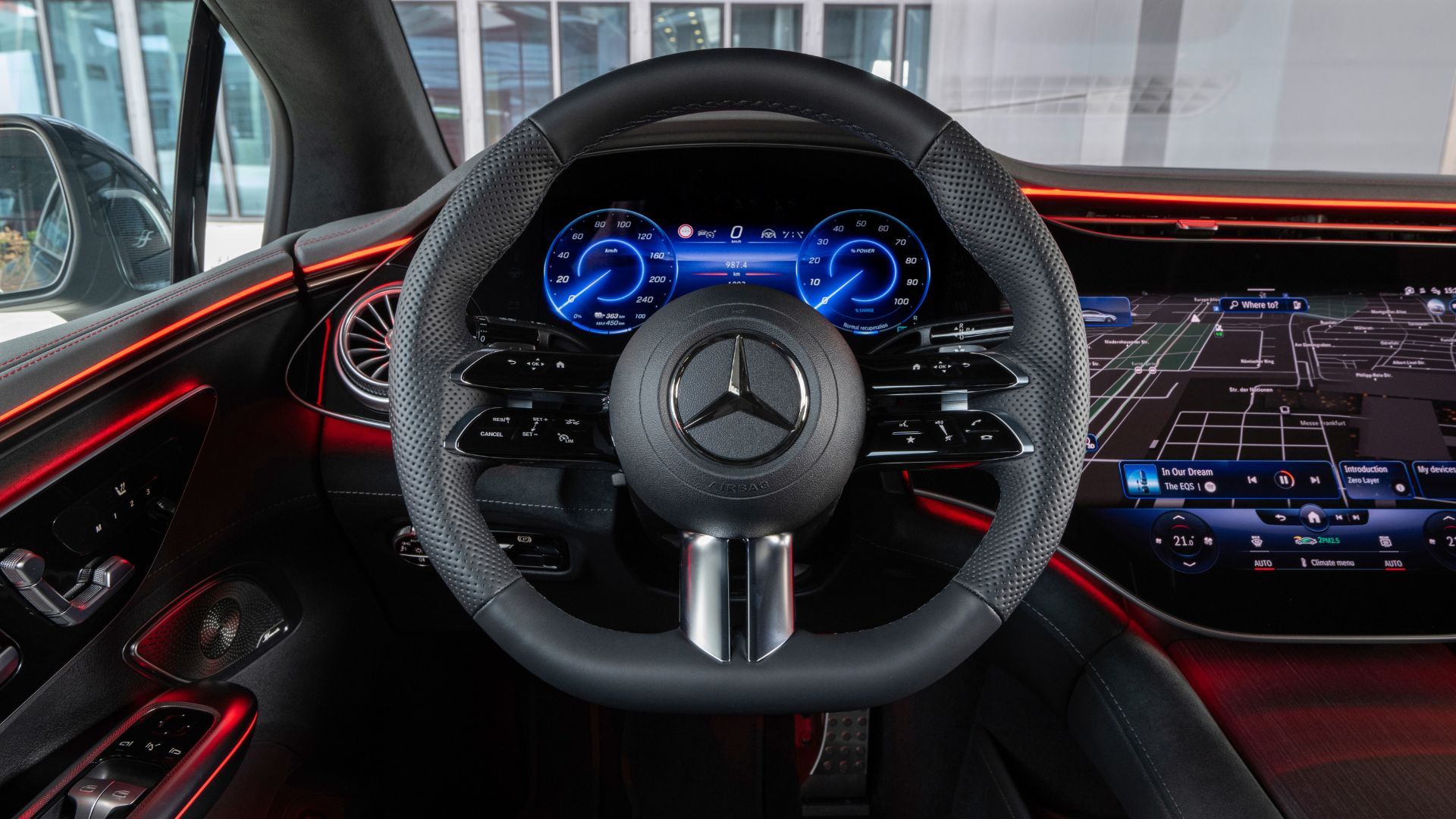 Close-up shot of the steering wheel in a Mercedes-Benz EQE, showing the digital instrum,ent cluster behind it, and the infotainment screen on the dashboard.
