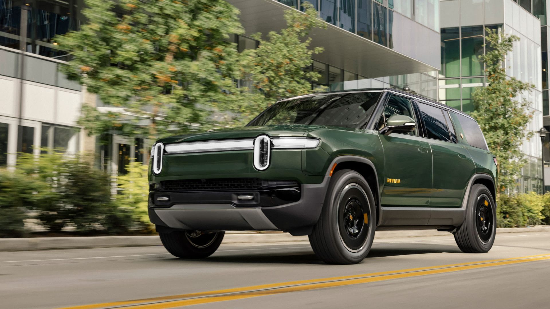 Dynamic front 3/4 shot of a green Rivian R1S driving in a city.