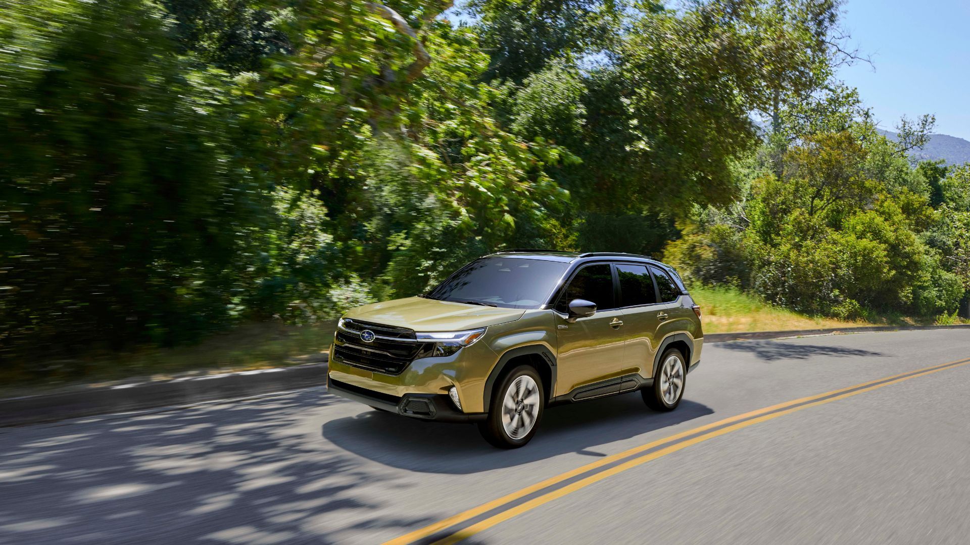 Dynamic front 3/4 shot of a green 2025 Subaru Forester Hybrid driving on a country road.