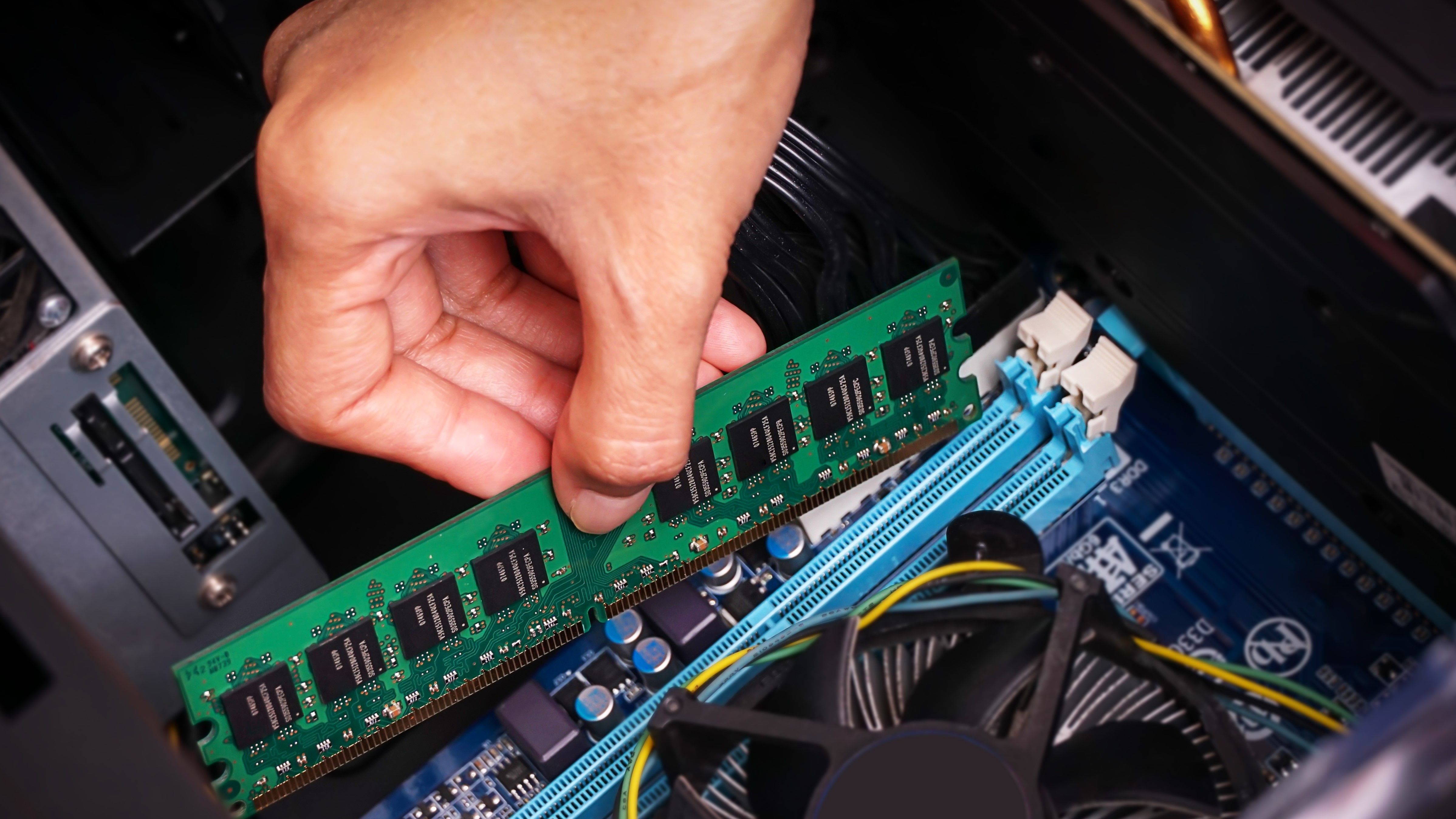 A persons hand pushing a stick of RAM into place inside a desktop PC.