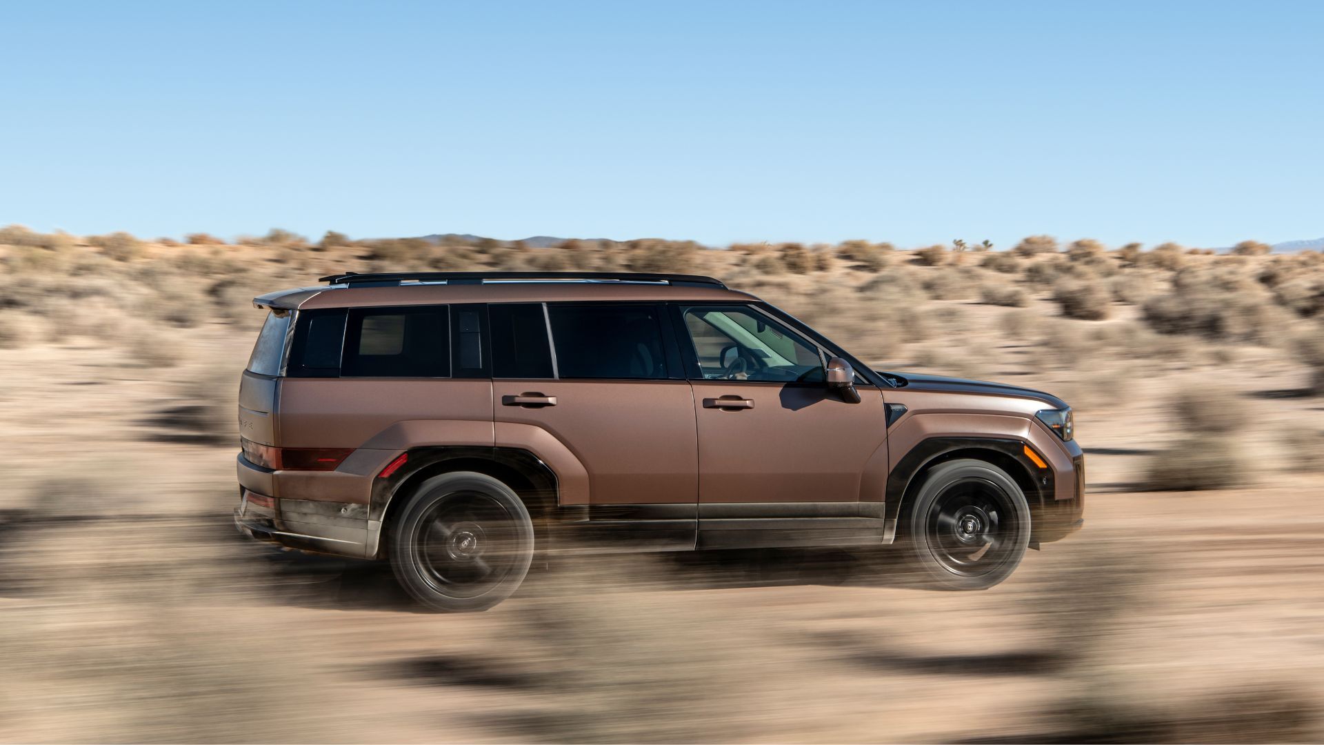 Dynamic side profile shot of a bronze 2025 Hyundai Santa Fe Hybrid off-roading in the desert.