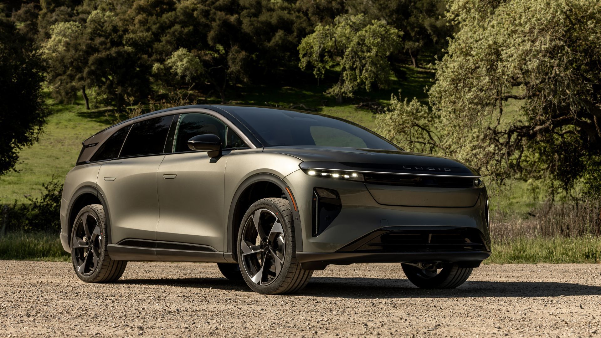 Static front 3/4 shot of a Lucid Gravity parked on gravel with trees in the background.