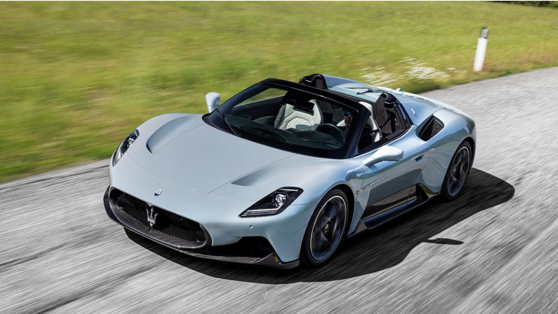 Dynamic front 3/4 shot of a gray Maserati MC20 Cielo driving on a country road.