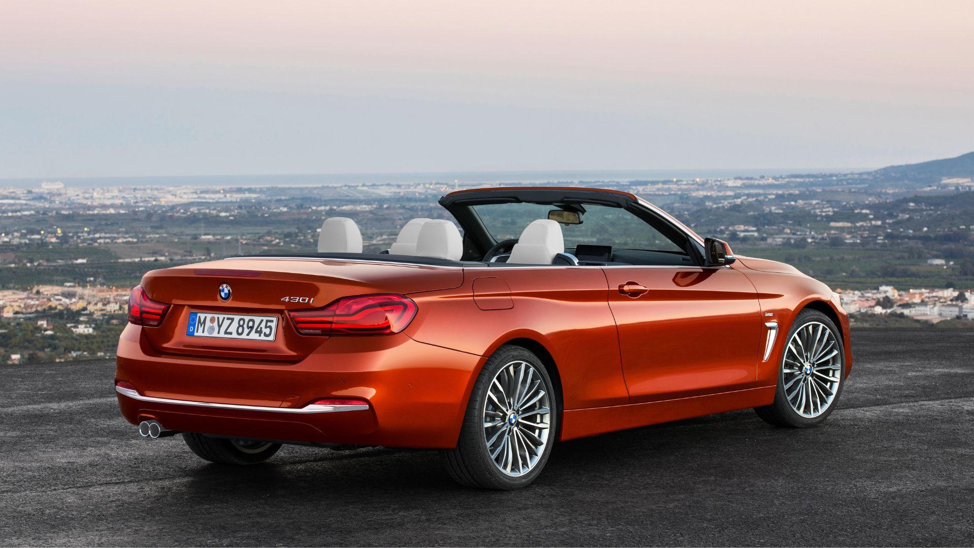 Static rear 3/4 shot of an orange 2017 BMW 430i Convertible with its roof folded down.