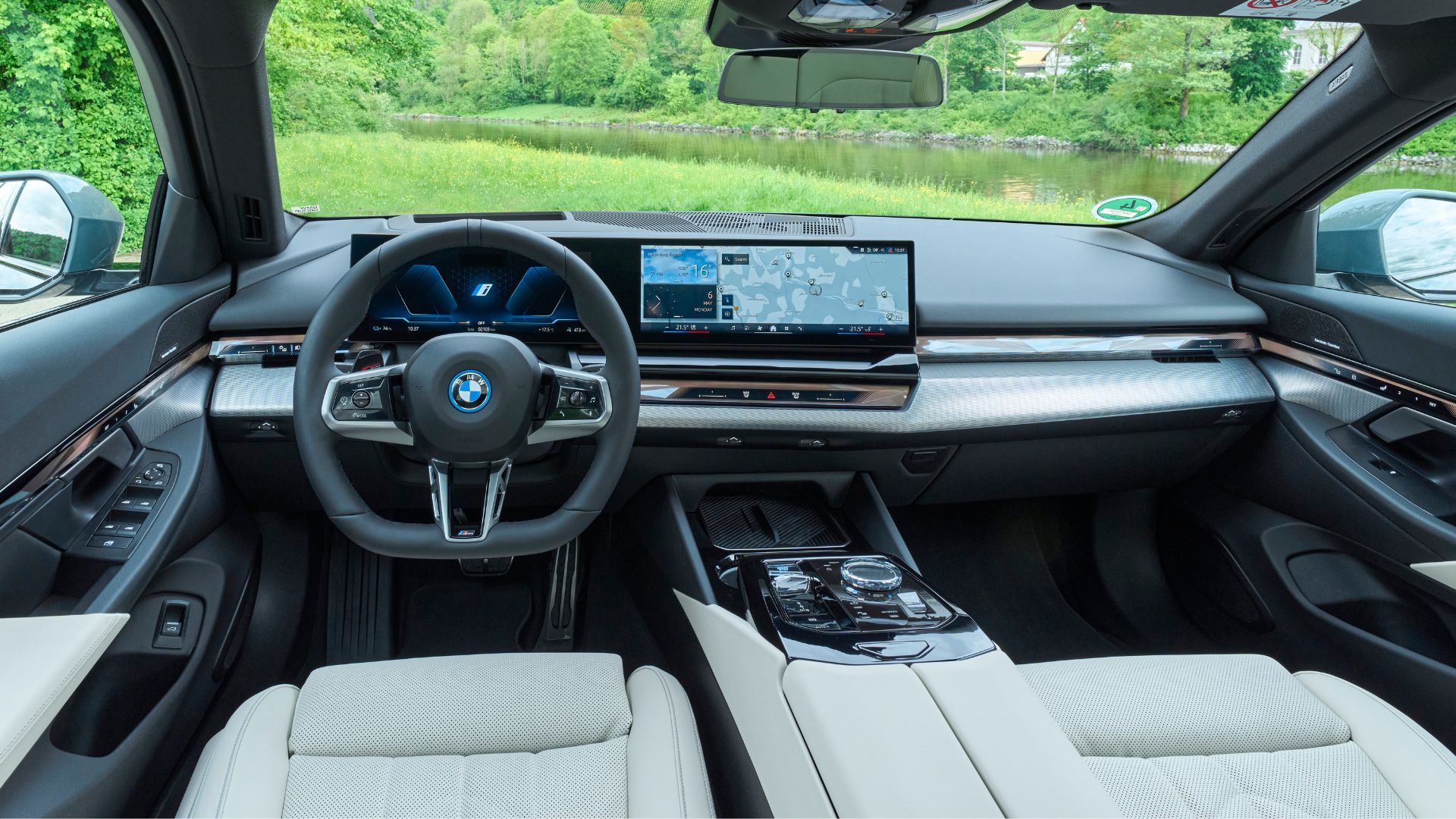 Shot inside the cabin of a BMW i5, showing the front seats, steering wheel, and infotainment screen.