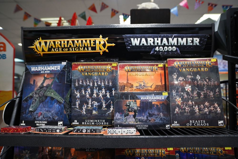 Store shelf with Warhammer 40,000 and Age of Sigmar boxed sets, dice, and game pieces.