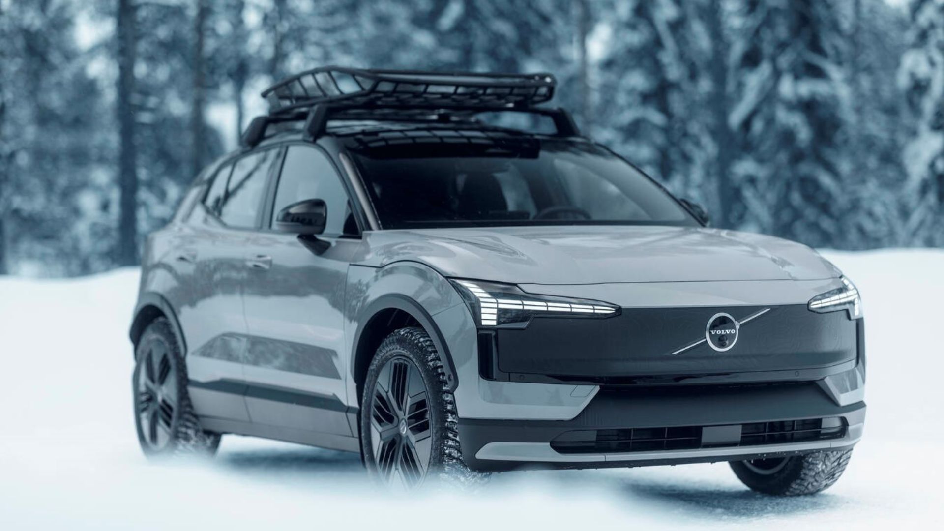 Dynamic front 3/4 shot of a silver Volvo EX30 Cross Country driving in the snow.