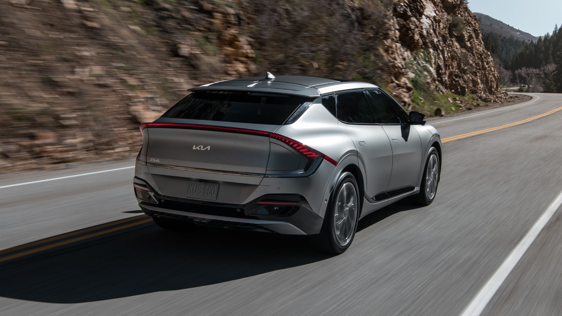 Dynamic rear 3/4 shot of a gray 2022 Kia EV6 driving on a winding road through the mountains.