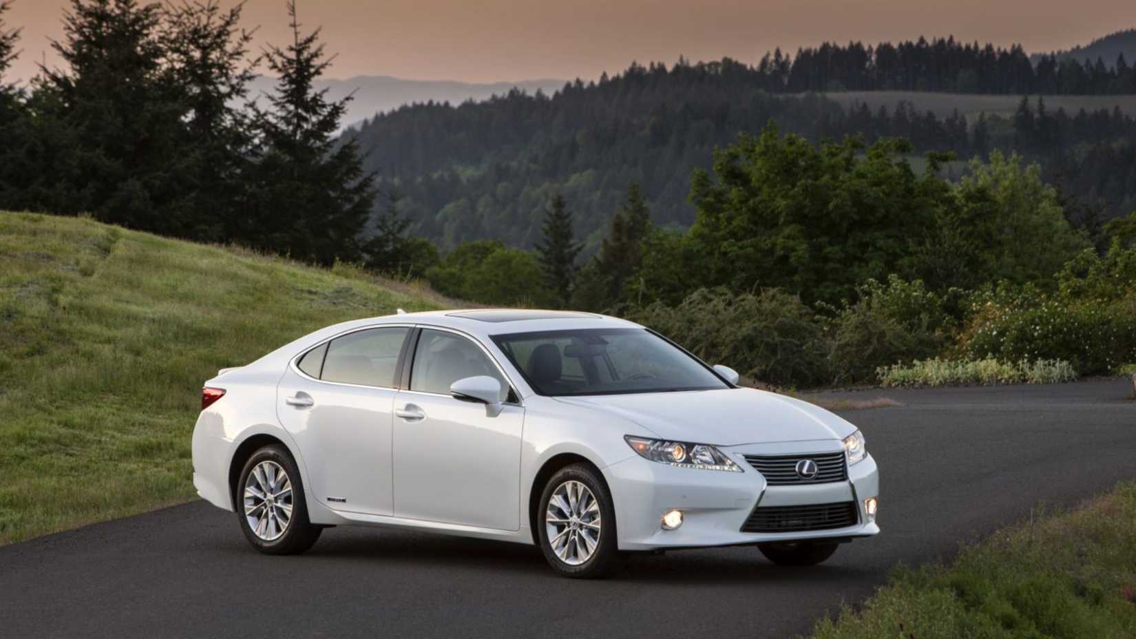 Static front 3/4 shot of a white 2015 Lexus ES 300h parked on tarmac with trees in the background.
